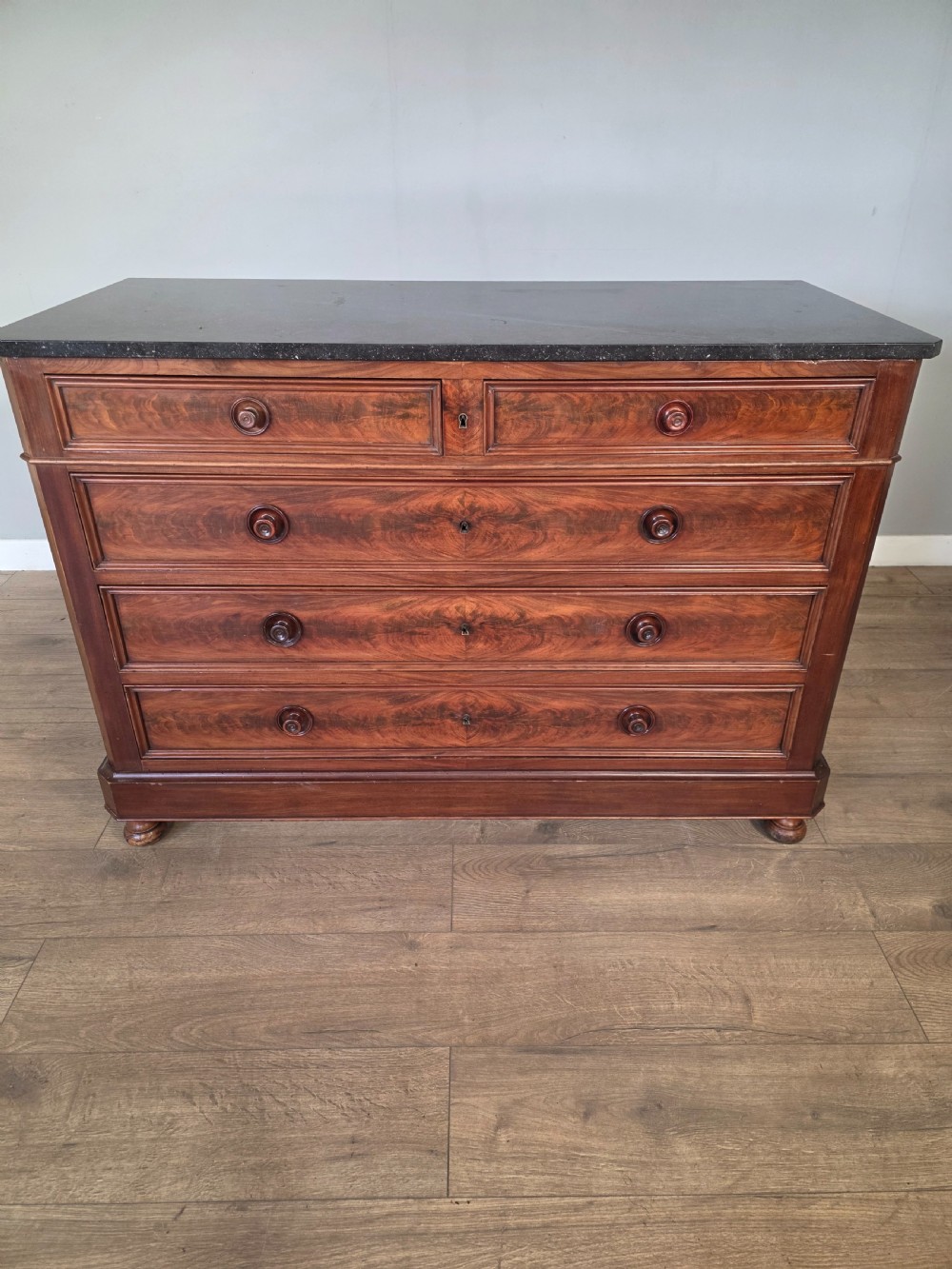 A nineteenth-century French mahogany chest of drawers featuring a dark marble top, flame mahogany drawer fronts, turned wooden knobs, and a plinth base. View II