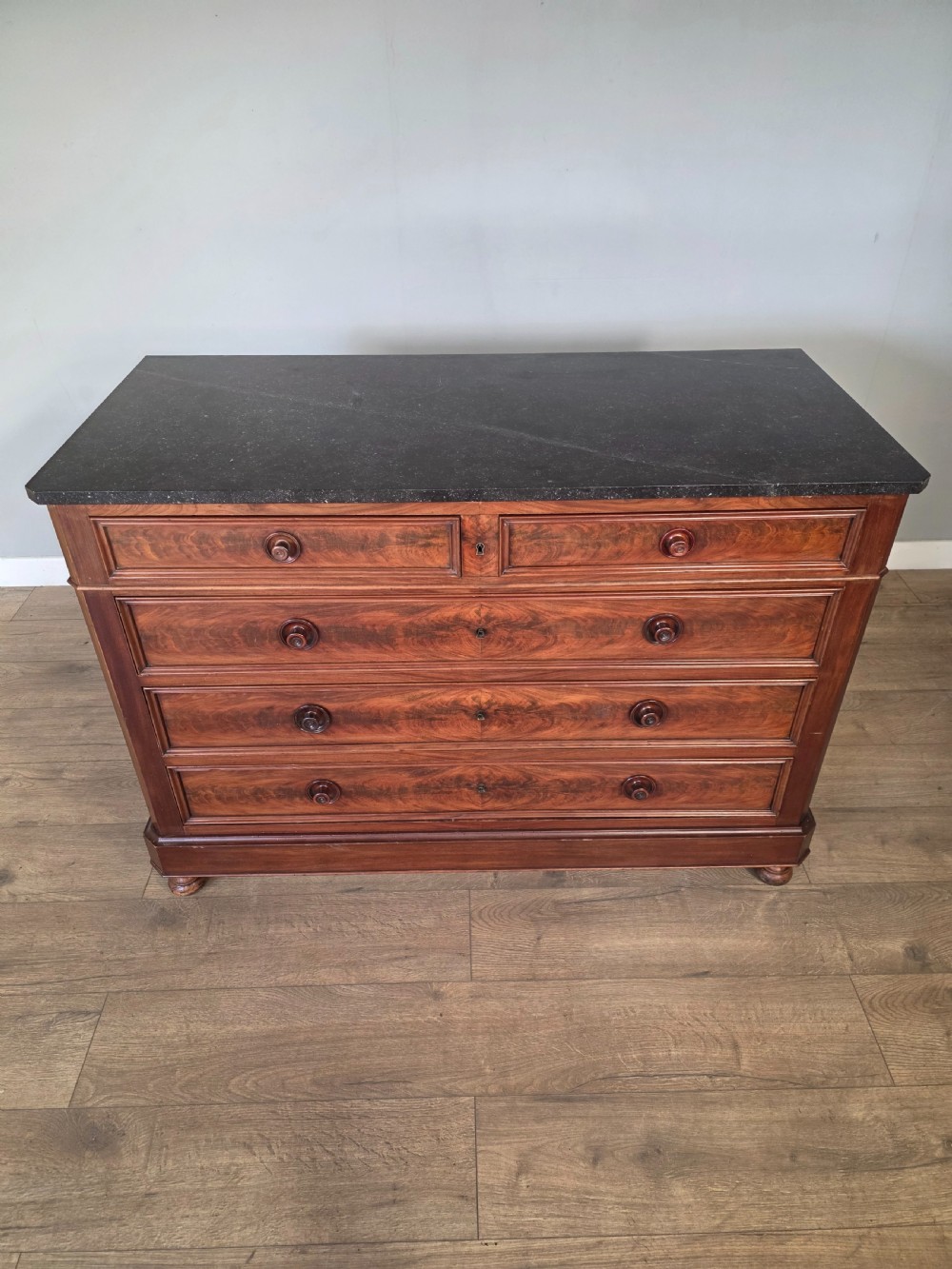 A nineteenth-century French mahogany chest of drawers featuring a dark marble top, flame mahogany drawer fronts, turned wooden knobs, and a plinth base. View III
