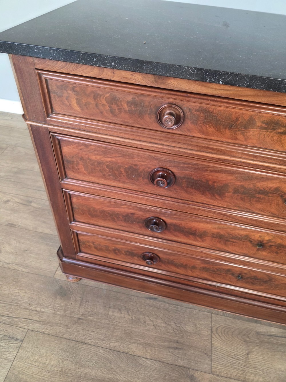 A nineteenth-century French mahogany chest of drawers featuring a dark marble top, flame mahogany drawer fronts, turned wooden knobs, and a plinth base. View VIII