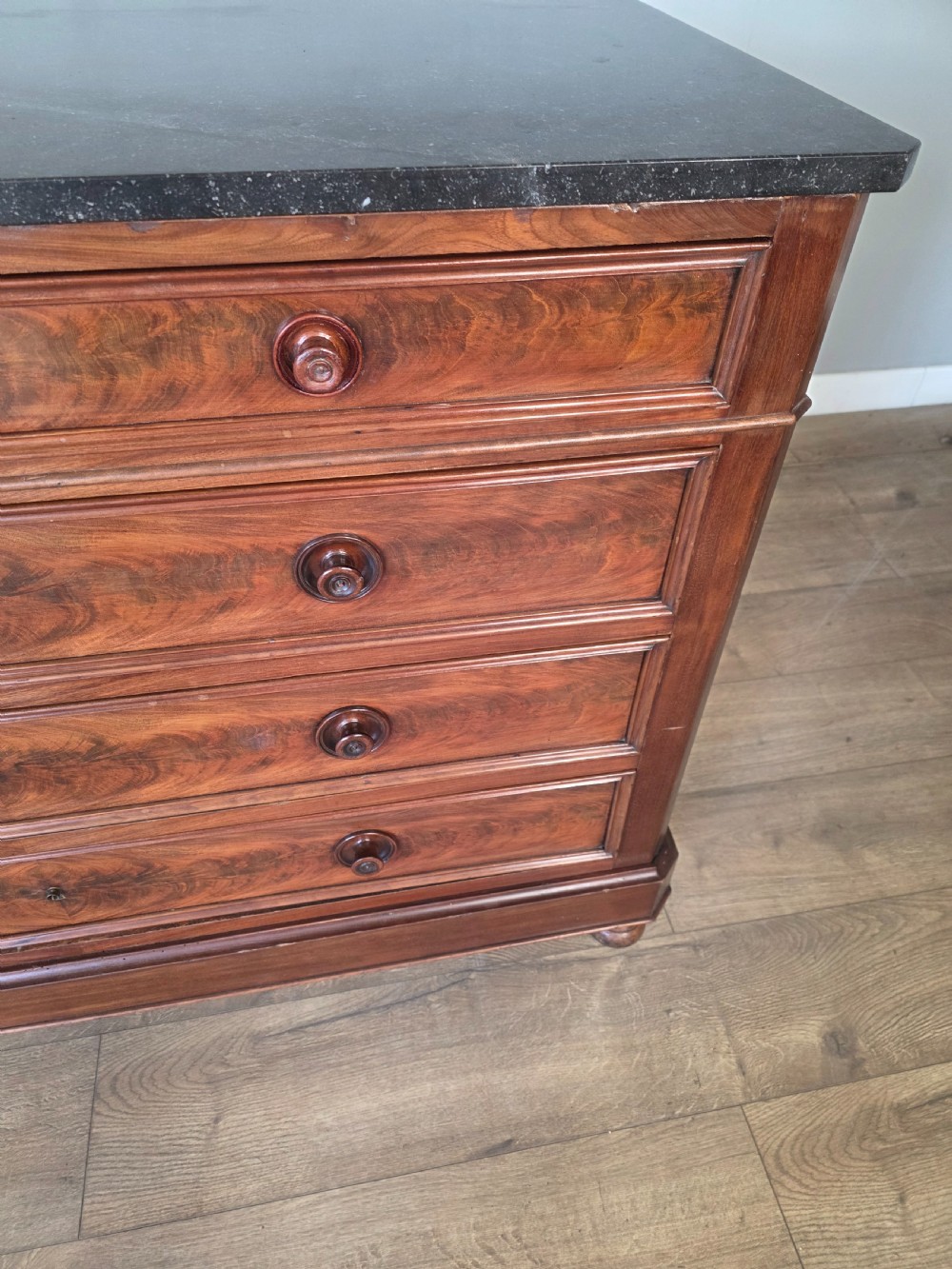 A nineteenth-century French mahogany chest of drawers featuring a dark marble top, flame mahogany drawer fronts, turned wooden knobs, and a plinth base. View IX