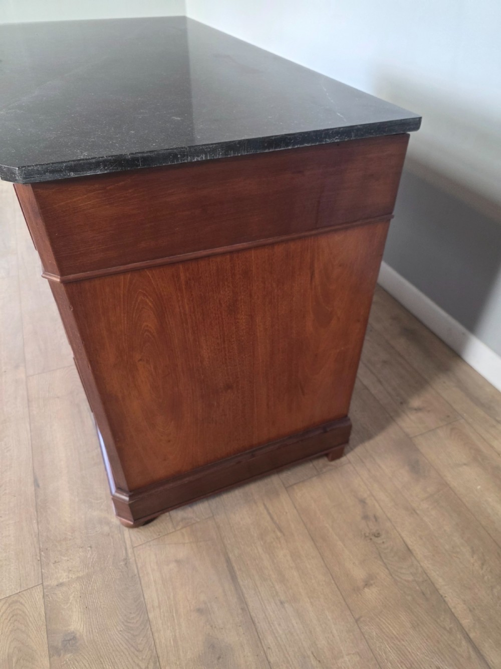 A nineteenth-century French mahogany chest of drawers featuring a dark marble top, flame mahogany drawer fronts, turned wooden knobs, and a plinth base. View XIII