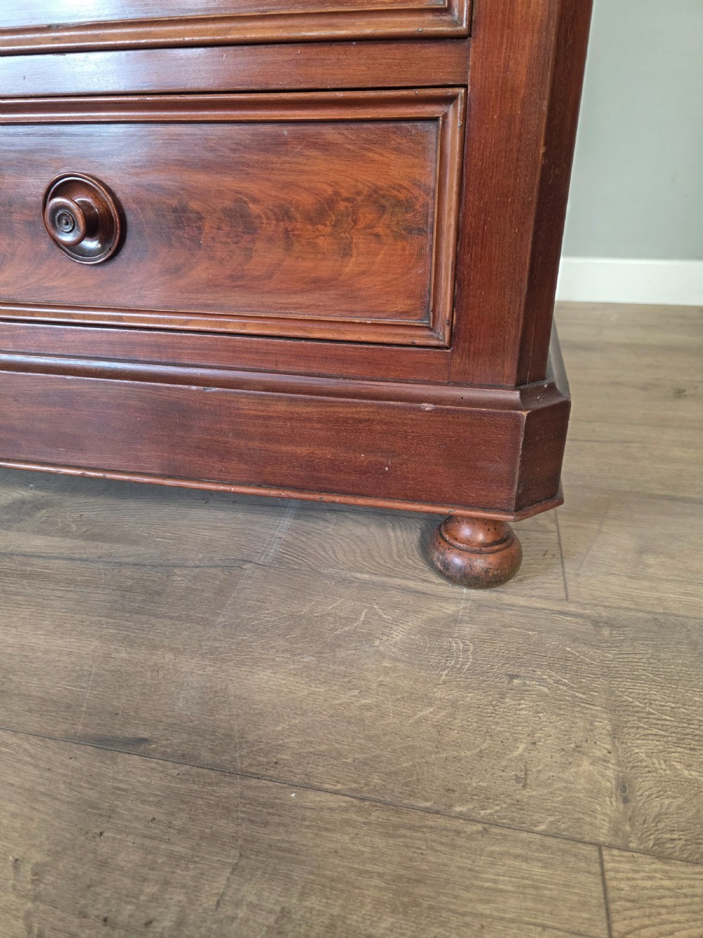 A nineteenth-century French mahogany chest of drawers featuring a dark marble top, flame mahogany drawer fronts, turned wooden knobs, and a plinth base. View XIX