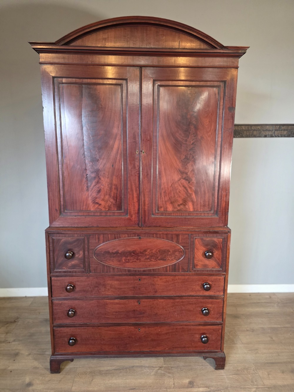 A late George III mahogany linen press featuring a double-door top cupboard under a arched pediment, resting on a lower section with drawers and bracket feet.