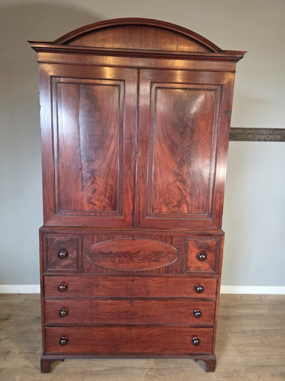 A late George III mahogany linen press featuring a double-door top cupboard under a arched pediment, resting on a lower section with drawers and bracket feet. View II