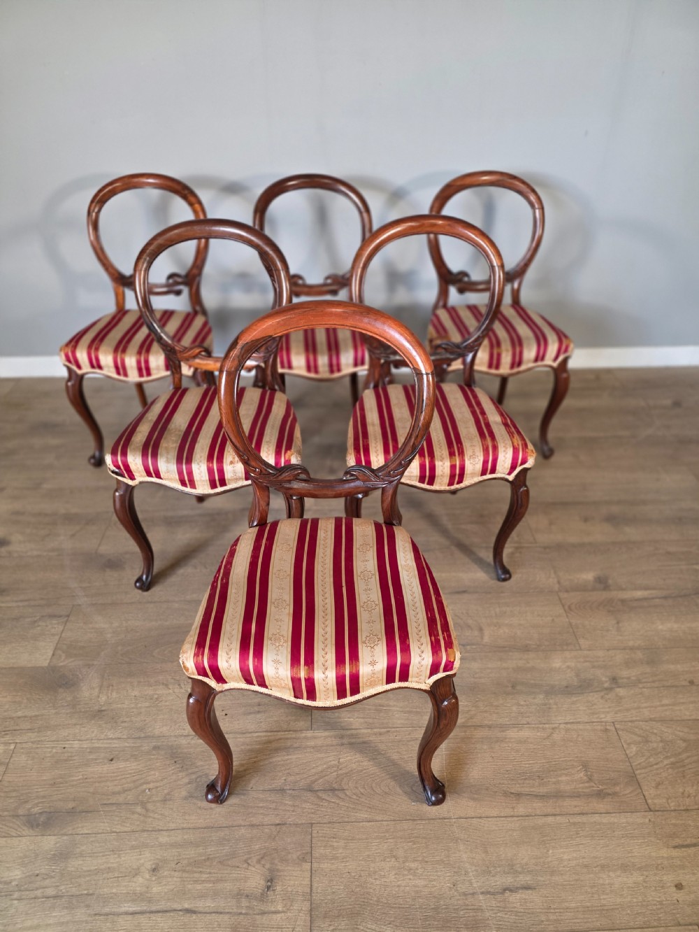 A set of six Victorian rosewood dining chairs featuring open balloon backs, carved waist rails, cabriole legs, and red and gold striped upholstered seats.