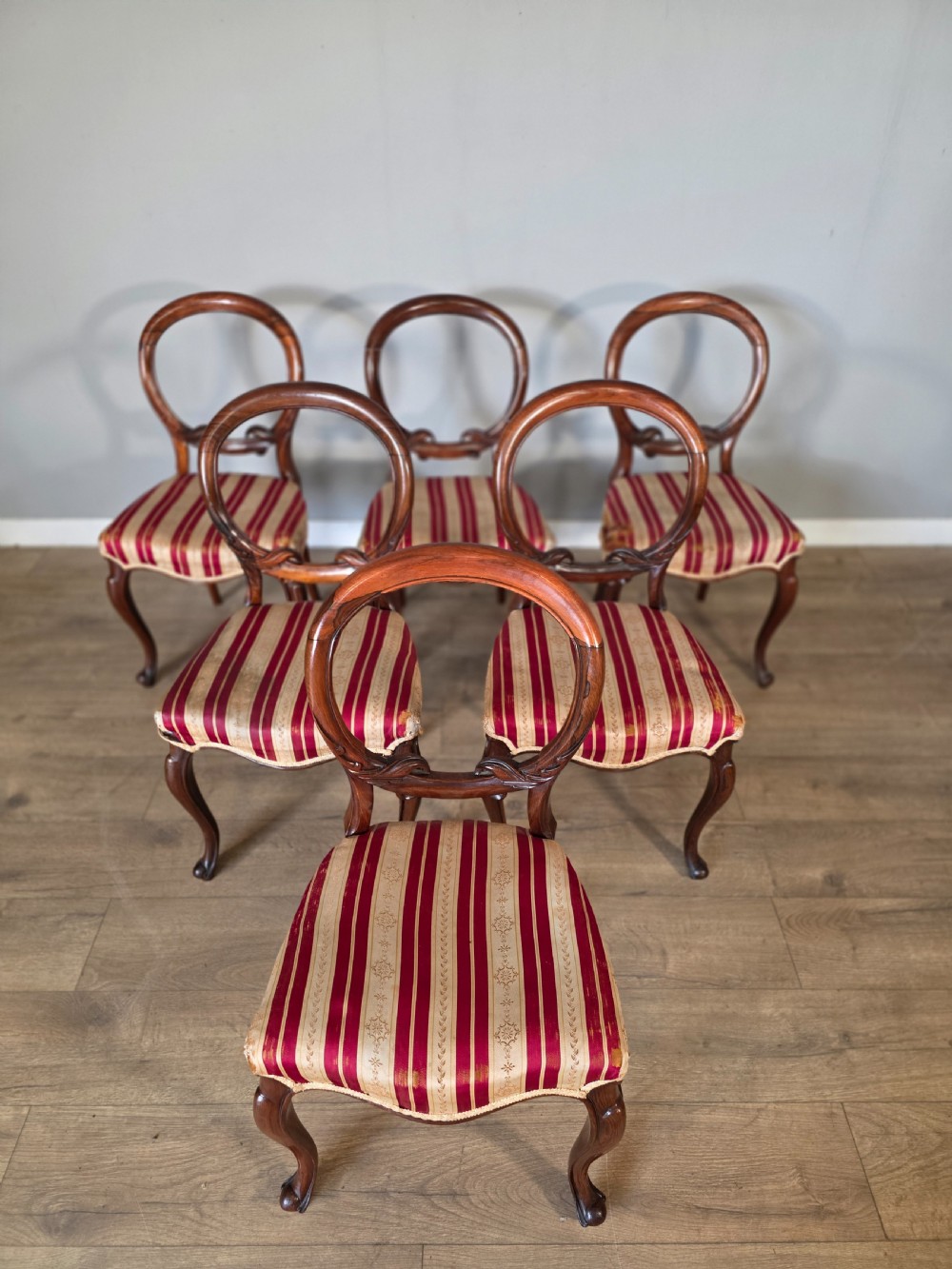 A set of six Victorian rosewood dining chairs featuring open balloon backs, carved waist rails, cabriole legs, and red and gold striped upholstered seats. View II
