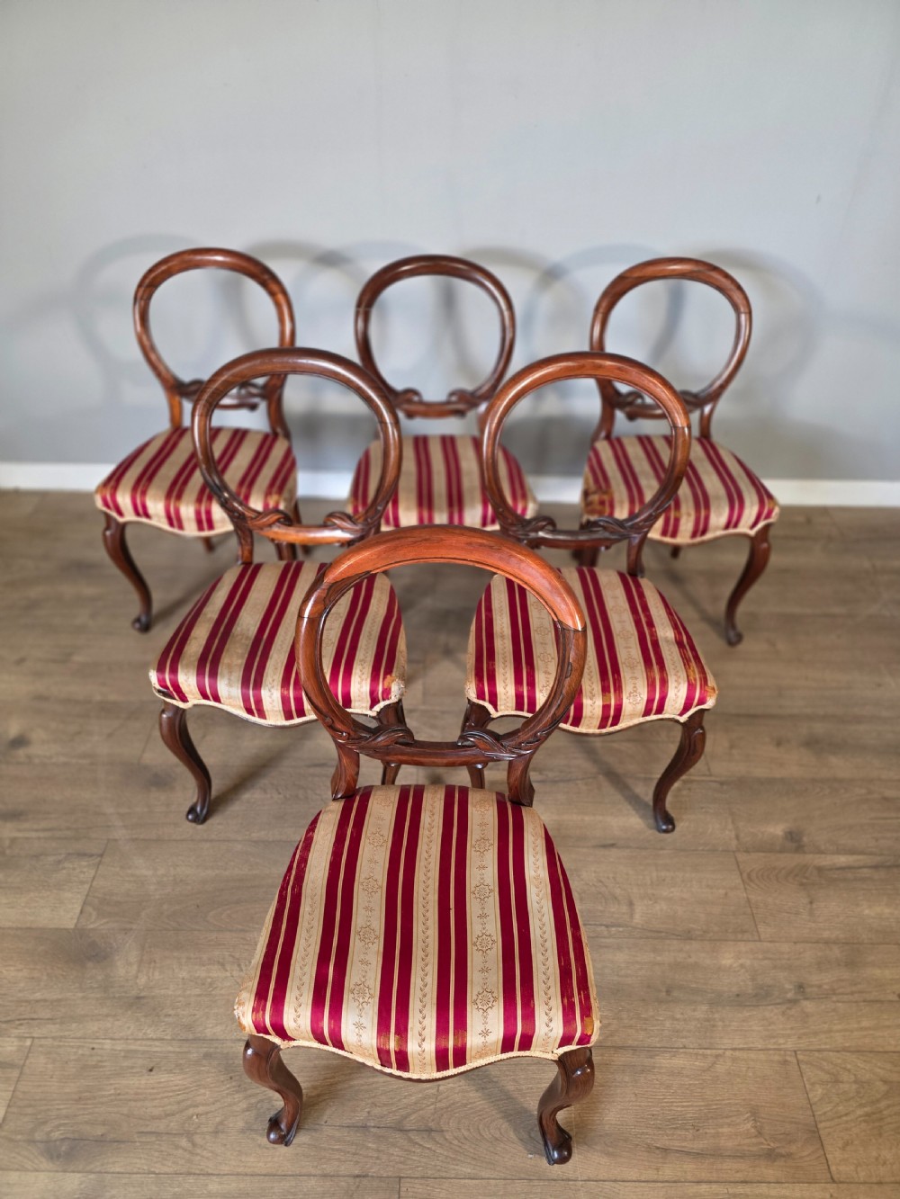 A set of six Victorian rosewood dining chairs featuring open balloon backs, carved waist rails, cabriole legs, and red and gold striped upholstered seats. View III