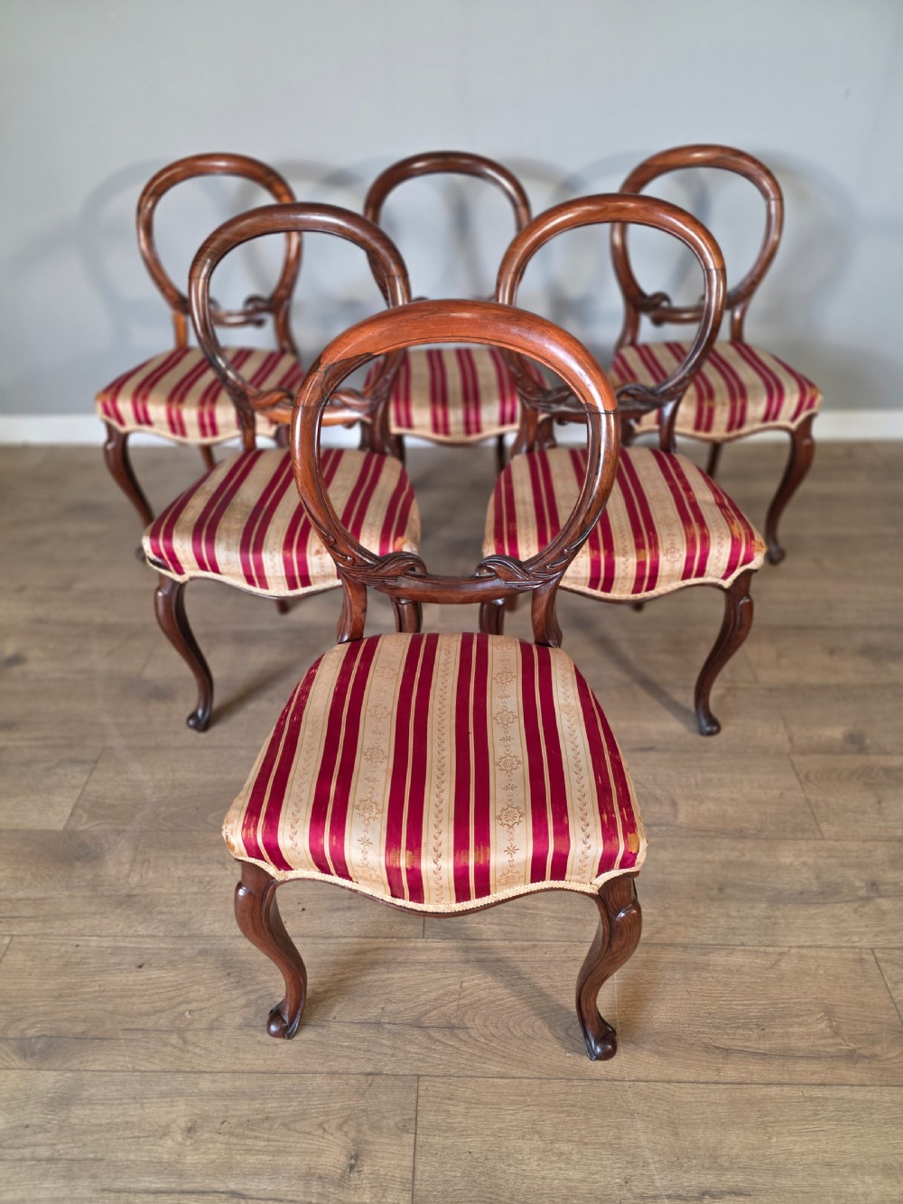 A set of six Victorian rosewood dining chairs featuring open balloon backs, carved waist rails, cabriole legs, and red and gold striped upholstered seats. View IV