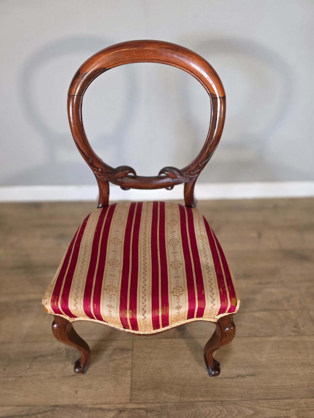 A set of six Victorian rosewood dining chairs featuring open balloon backs, carved waist rails, cabriole legs, and red and gold striped upholstered seats. View VI