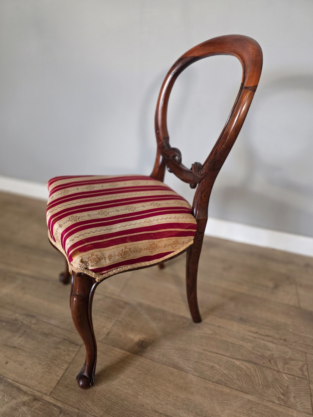 A set of six Victorian rosewood dining chairs featuring open balloon backs, carved waist rails, cabriole legs, and red and gold striped upholstered seats. View VIII