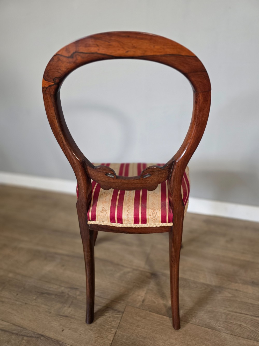 A set of six Victorian rosewood dining chairs featuring open balloon backs, carved waist rails, cabriole legs, and red and gold striped upholstered seats. View IX