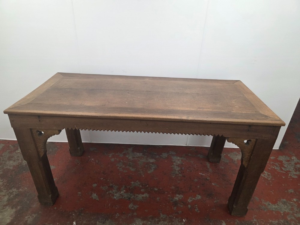 A rectangular dark oak console table featuring a notched dentil apron, carved corner spandrels, and sturdy chamfered legs.