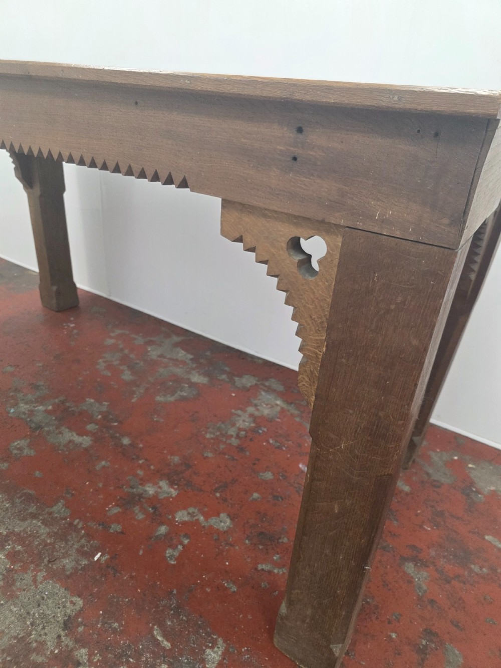 A rectangular dark oak console table featuring a notched dentil apron, carved corner spandrels, and sturdy chamfered legs. View V