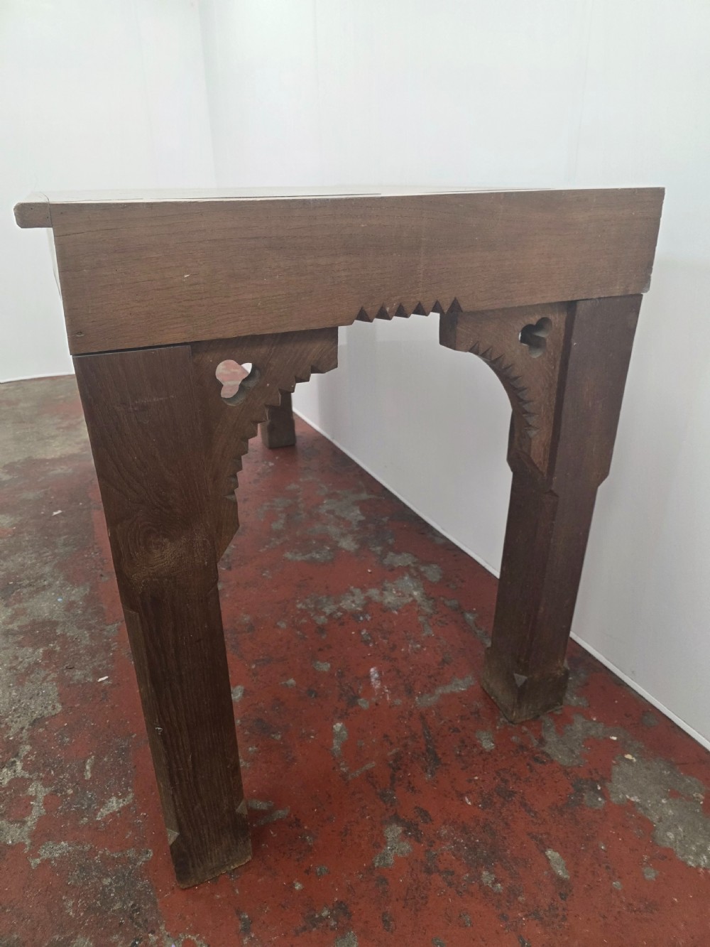 A rectangular dark oak console table featuring a notched dentil apron, carved corner spandrels, and sturdy chamfered legs. View VI