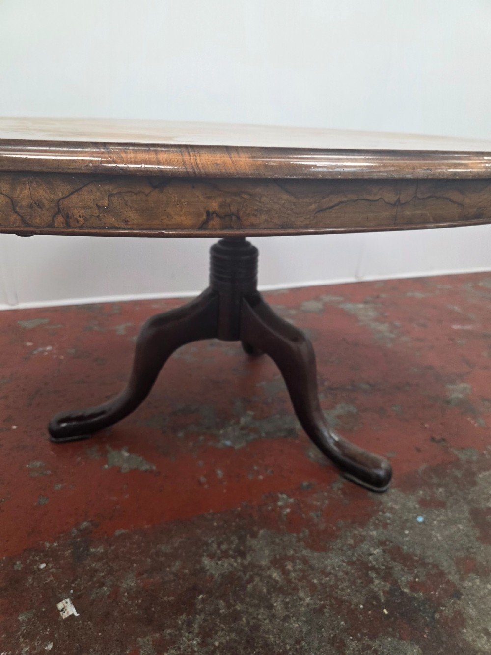 An oval low coffee table featuring a figured burr walnut top set on a dark cast iron tripod base. View VI
