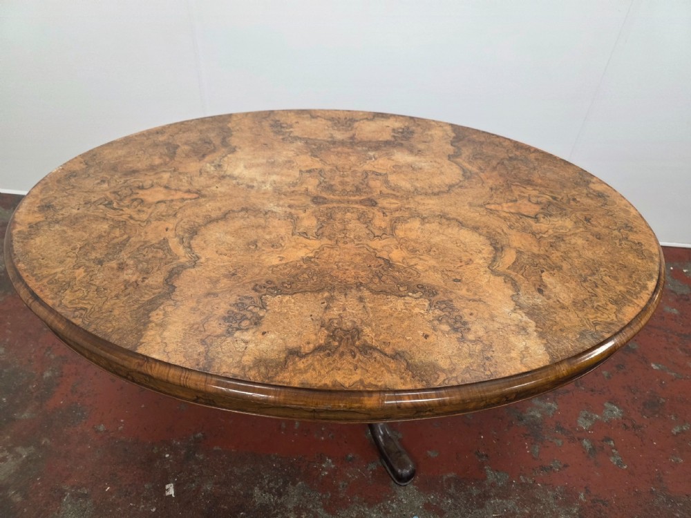 An oval low coffee table featuring a figured burr walnut top set on a dark cast iron tripod base. View IX