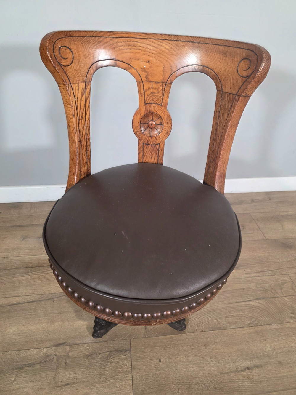 An antique 1890s swivel chair featuring a carved oak backrest, brown leather studded seat, and a cast iron pedestal base. View II
