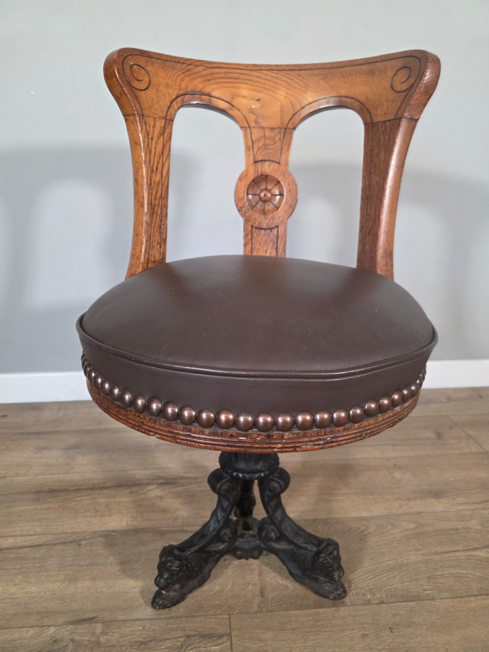 An antique 1890s swivel chair featuring a carved oak backrest, brown leather studded seat, and a cast iron pedestal base. View III