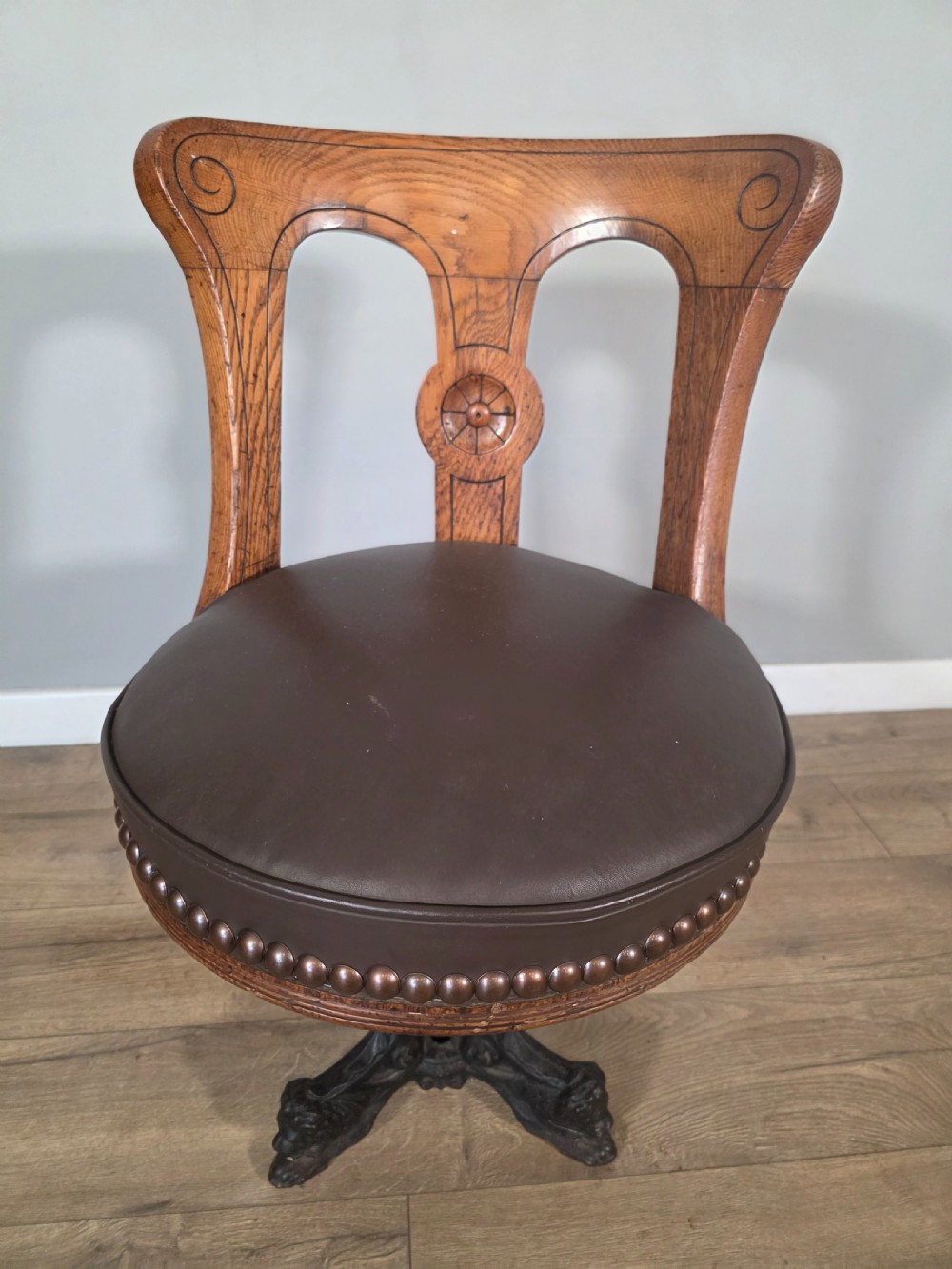 An antique 1890s swivel chair featuring a carved oak backrest, brown leather studded seat, and a cast iron pedestal base. View IV