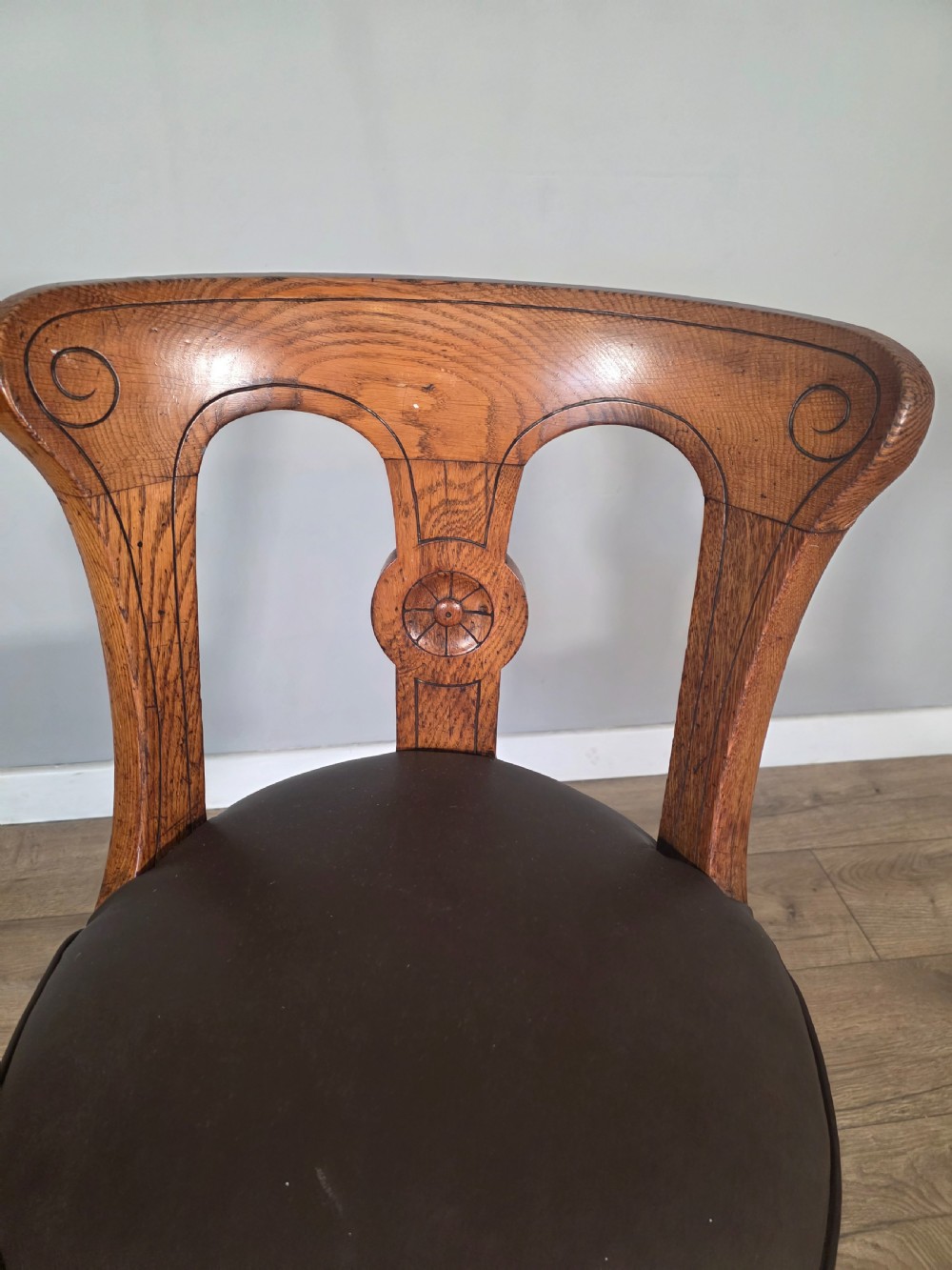 An antique 1890s swivel chair featuring a carved oak backrest, brown leather studded seat, and a cast iron pedestal base. View VI