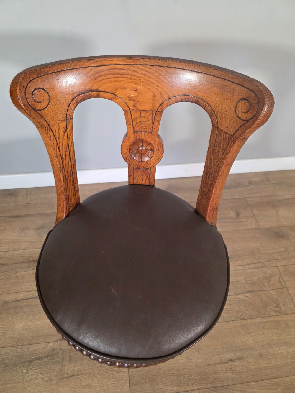 An antique 1890s swivel chair featuring a carved oak backrest, brown leather studded seat, and a cast iron pedestal base. View VII