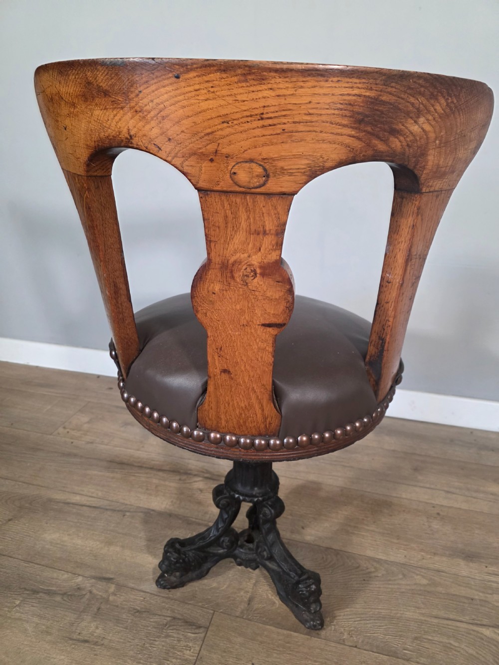An antique 1890s swivel chair featuring a carved oak backrest, brown leather studded seat, and a cast iron pedestal base. View VIII