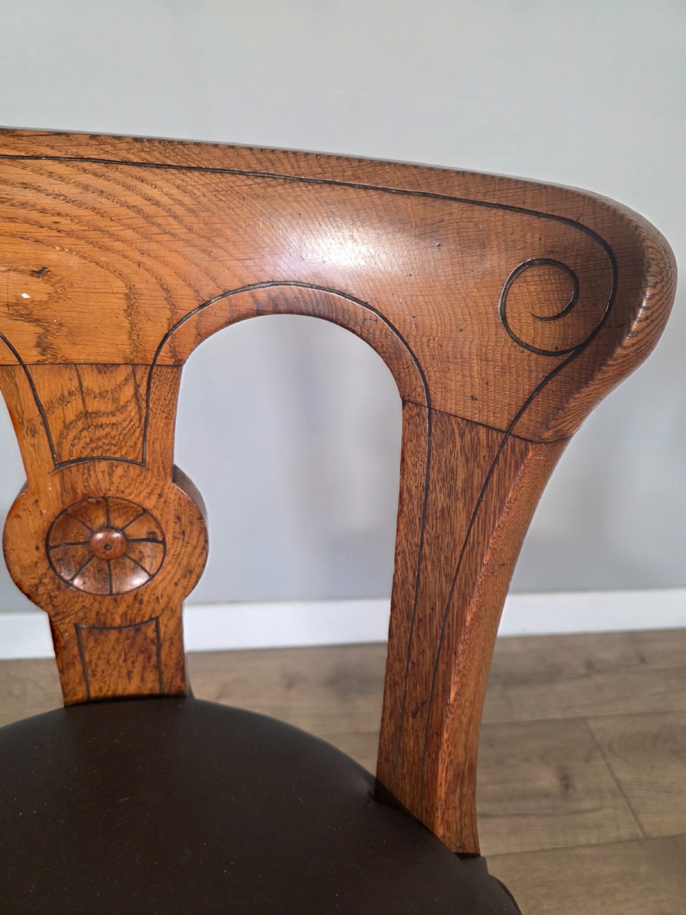 An antique 1890s swivel chair featuring a carved oak backrest, brown leather studded seat, and a cast iron pedestal base. View X