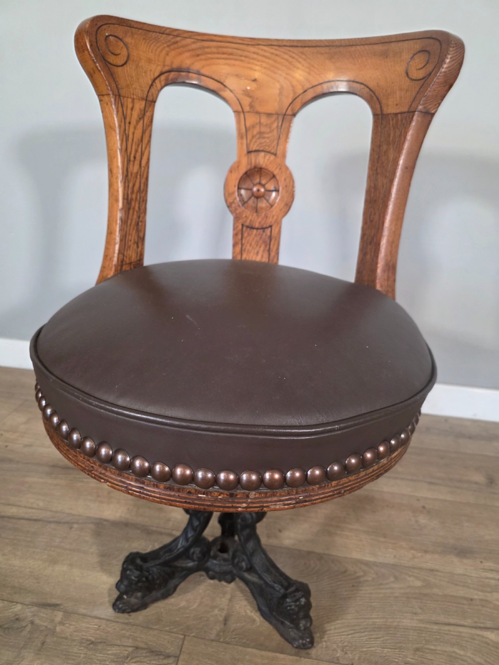 An antique 1890s swivel chair featuring a carved oak backrest, brown leather studded seat, and a cast iron pedestal base. View XI