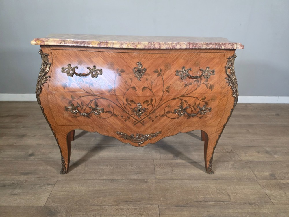 A French Louis XV style bombe commode featuring floral marquetry wood inlays, gilded metal mounts, cabriole legs, and a shaped pink-variegated marble top.