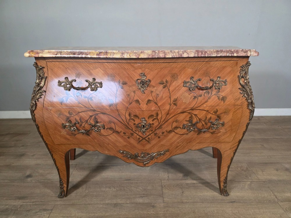 A French Louis XV style bombe commode featuring floral marquetry wood inlays, gilded metal mounts, cabriole legs, and a shaped pink-variegated marble top. View II