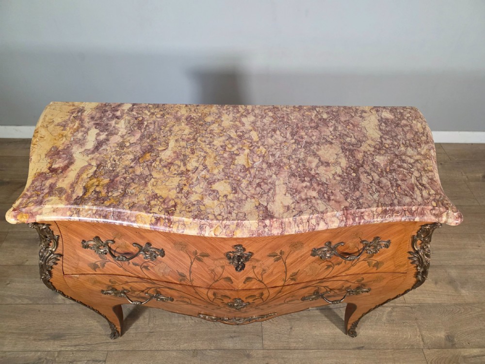 A French Louis XV style bombe commode featuring floral marquetry wood inlays, gilded metal mounts, cabriole legs, and a shaped pink-variegated marble top. View V