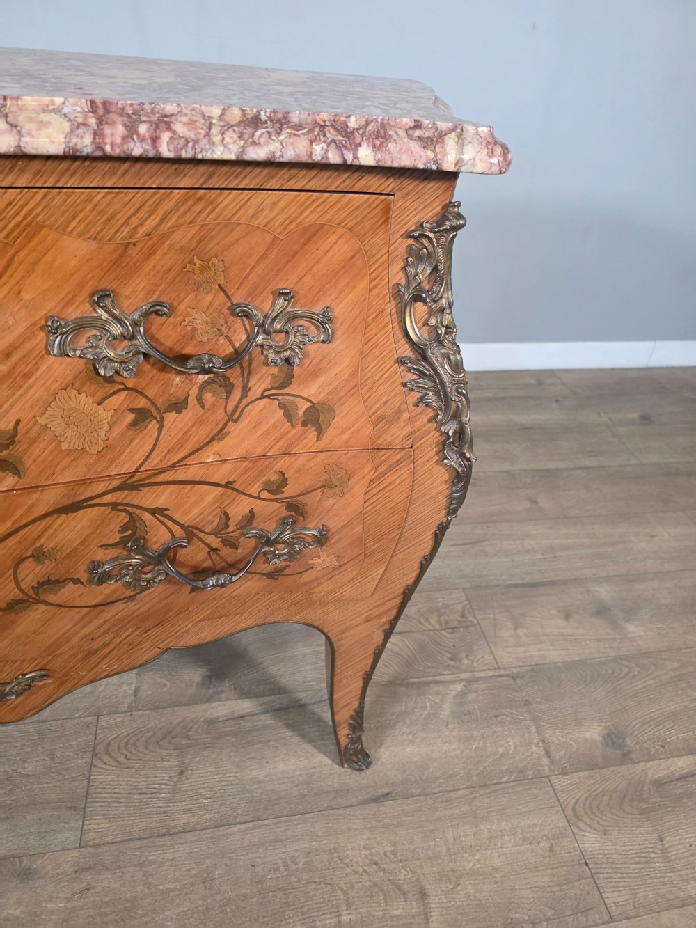 A French Louis XV style bombe commode featuring floral marquetry wood inlays, gilded metal mounts, cabriole legs, and a shaped pink-variegated marble top. View VIII