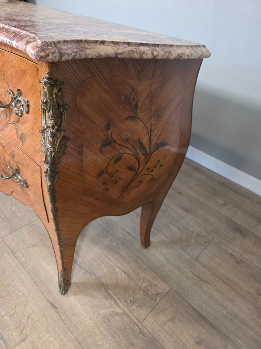 A French Louis XV style bombe commode featuring floral marquetry wood inlays, gilded metal mounts, cabriole legs, and a shaped pink-variegated marble top. View X