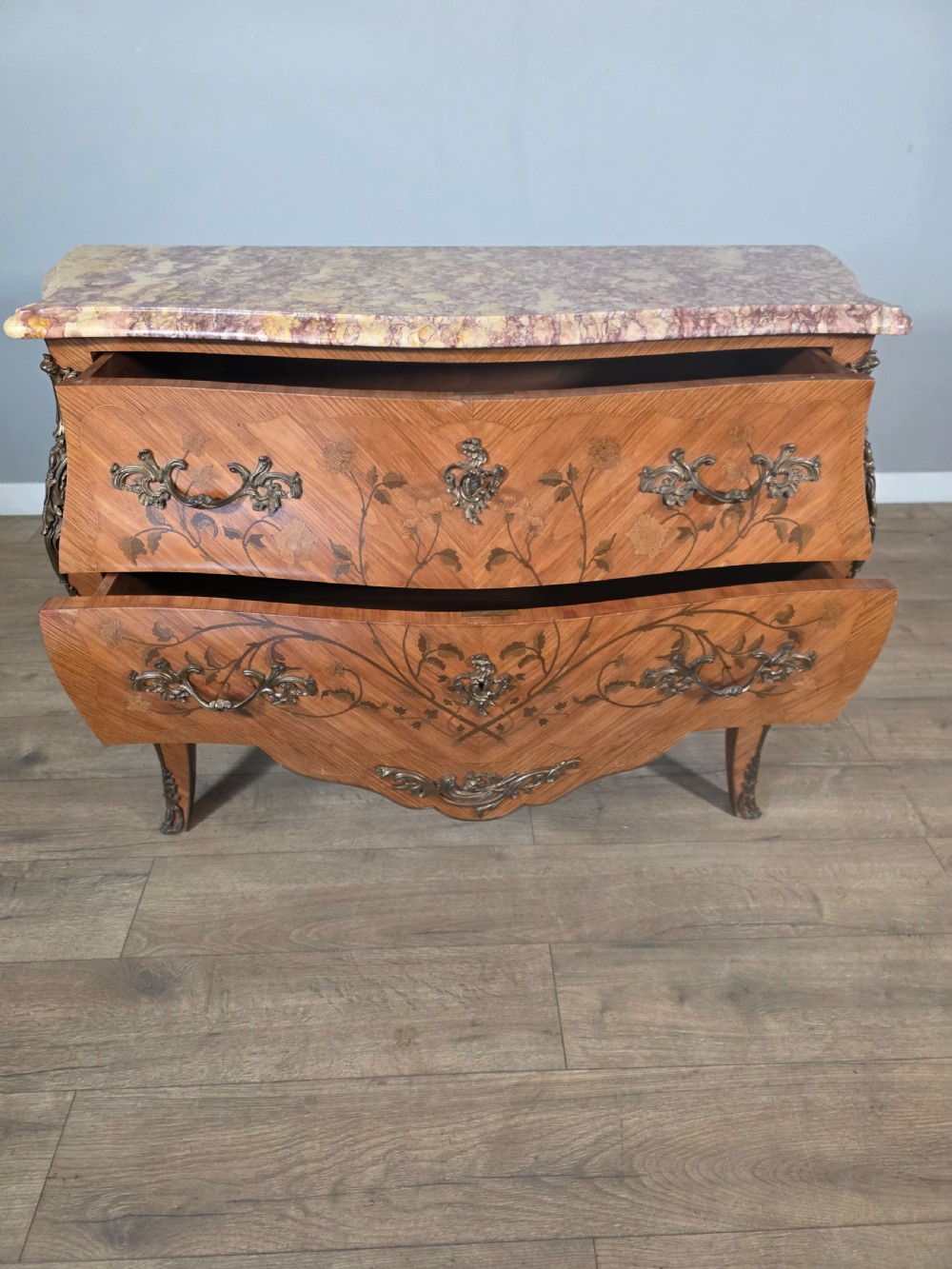 A French Louis XV style bombe commode featuring floral marquetry wood inlays, gilded metal mounts, cabriole legs, and a shaped pink-variegated marble top. View XII