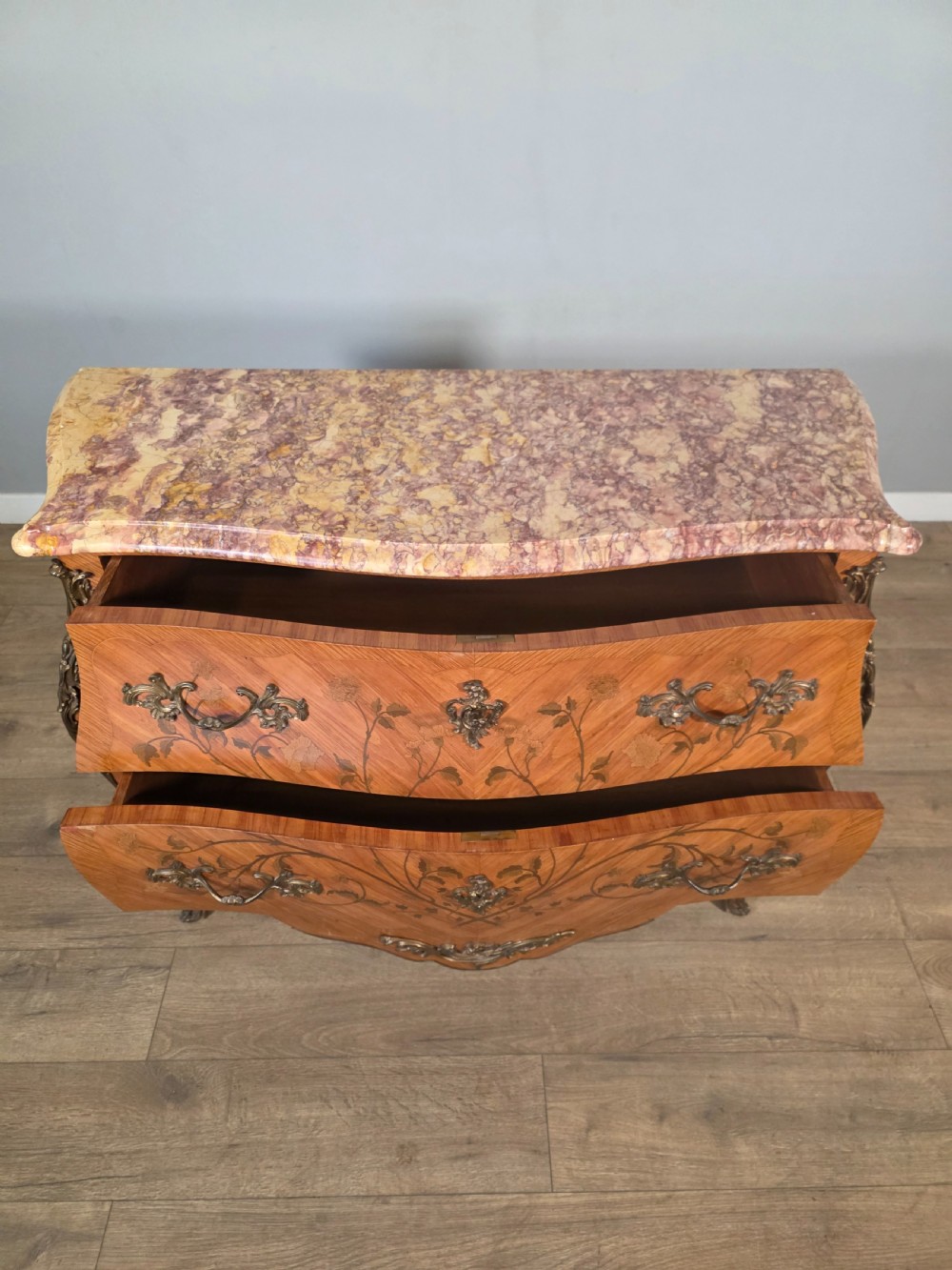 A French Louis XV style bombe commode featuring floral marquetry wood inlays, gilded metal mounts, cabriole legs, and a shaped pink-variegated marble top. View XIII