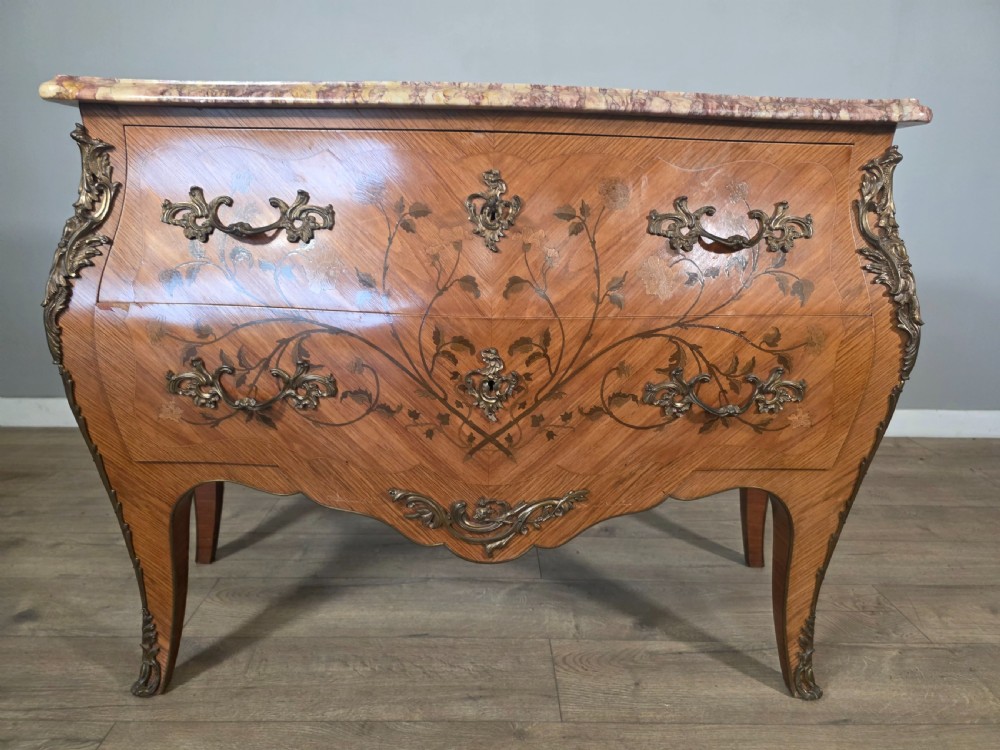 A French Louis XV style bombe commode featuring floral marquetry wood inlays, gilded metal mounts, cabriole legs, and a shaped pink-variegated marble top. View XVI