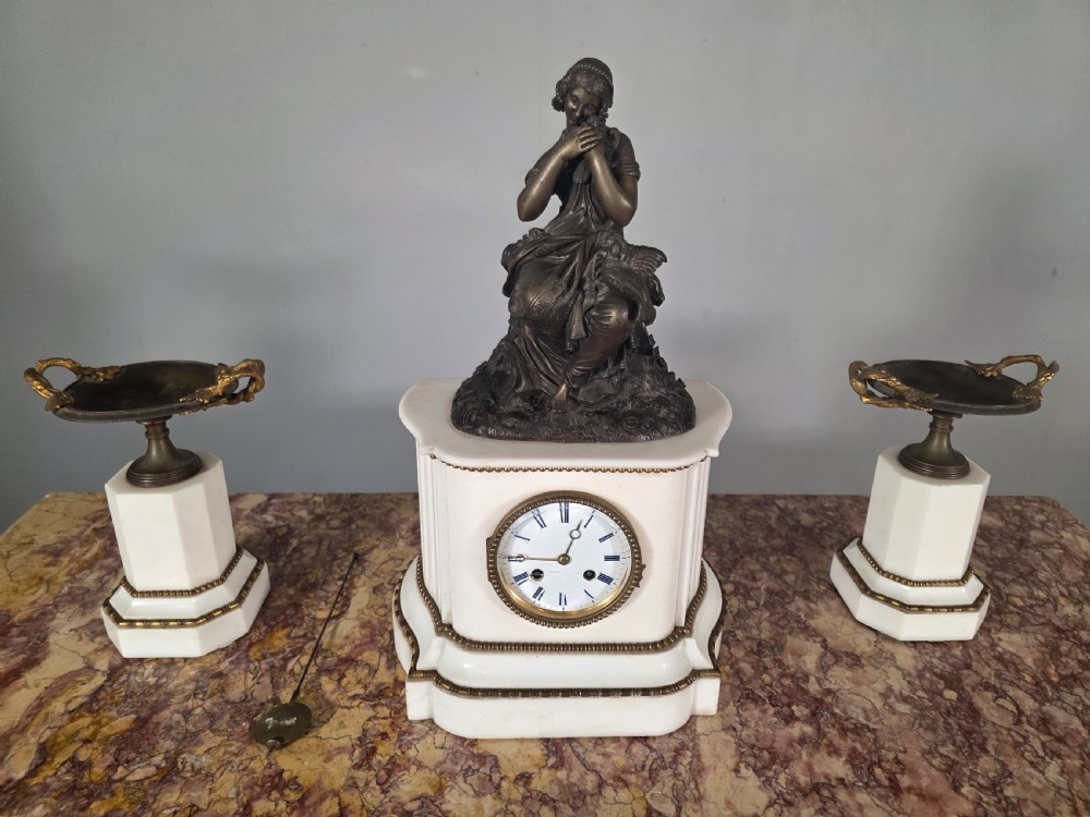 A late 19th-century French white marble mantel clock set featuring a patinated bronze seated female figure surmount, flanked by two matching marble tazze.