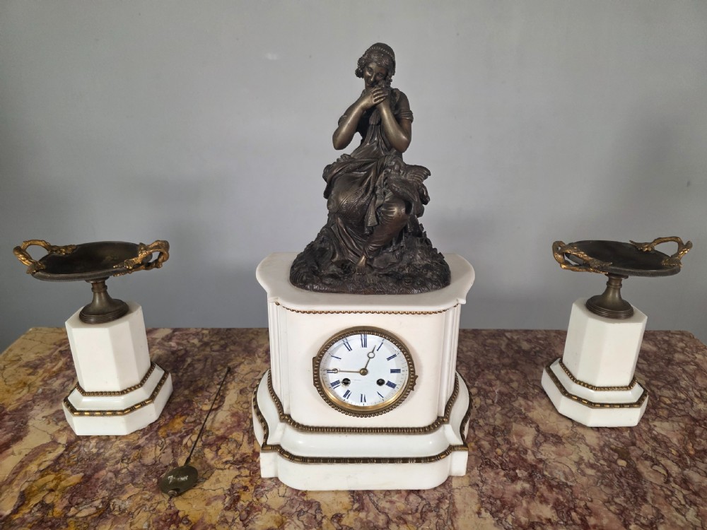 A late 19th-century French white marble mantel clock set featuring a patinated bronze seated female figure surmount, flanked by two matching marble tazze. View II