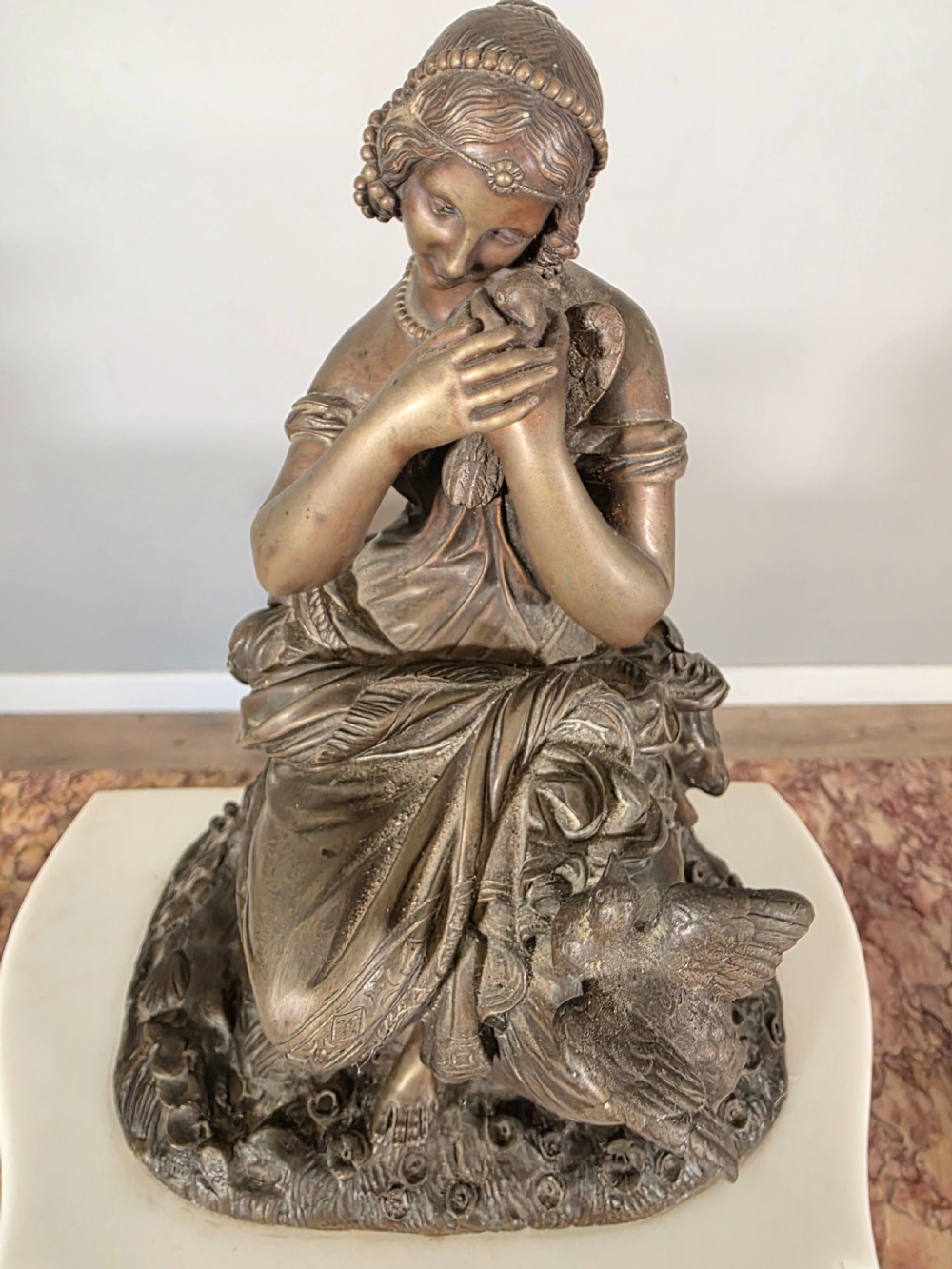 A late 19th-century French white marble mantel clock set featuring a patinated bronze seated female figure surmount, flanked by two matching marble tazze. View X