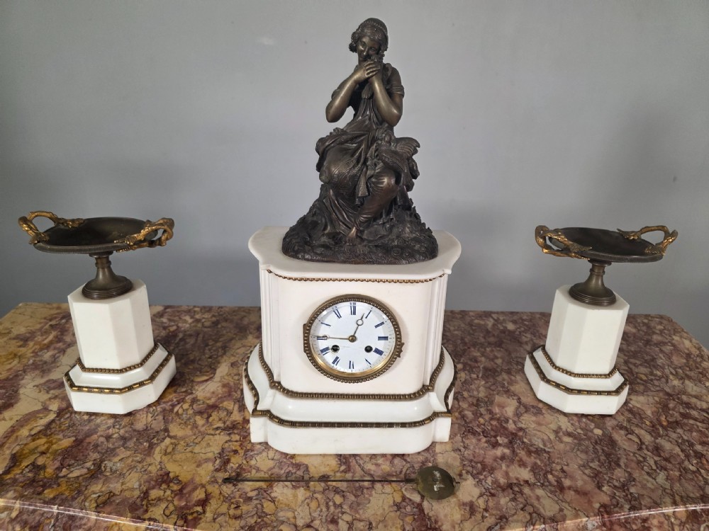 A late 19th-century French white marble mantel clock set featuring a patinated bronze seated female figure surmount, flanked by two matching marble tazze. View XIV