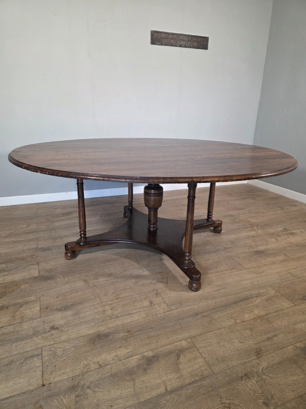 A large antique oval oak dining table featuring turned legs and a central stretcher base.