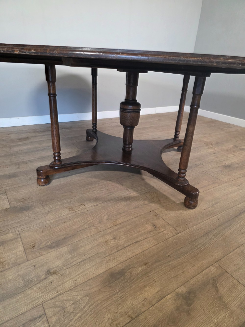 A large antique oval oak dining table featuring turned legs and a central stretcher base. View VI