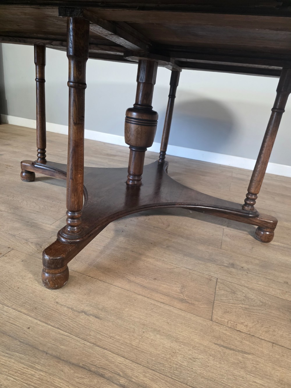 A large antique oval oak dining table featuring turned legs and a central stretcher base. View VII