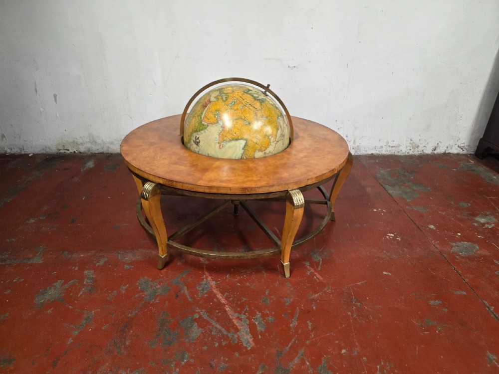 A circular mid-century coffee table featuring a central integrated terrestrial globe set within a honey brown wood veneer top, supported by curved legs and a brass framework.