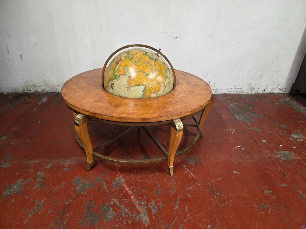 A circular mid-century coffee table featuring a central integrated terrestrial globe set within a honey brown wood veneer top, supported by curved legs and a brass framework. View II
