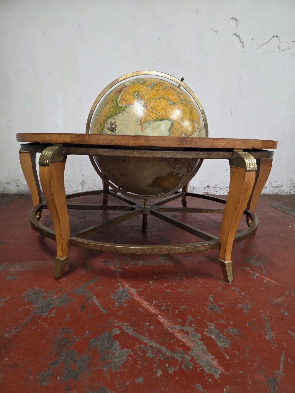A circular mid-century coffee table featuring a central integrated terrestrial globe set within a honey brown wood veneer top, supported by curved legs and a brass framework. View III