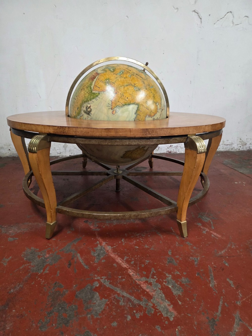 A circular mid-century coffee table featuring a central integrated terrestrial globe set within a honey brown wood veneer top, supported by curved legs and a brass framework. View IV