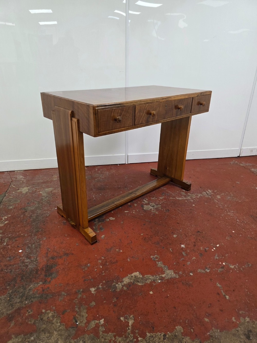 A 1930s Art Deco walnut desk featuring a rectangular top with three drawers, flat slab-style end legs, and a low cross stretcher. View II