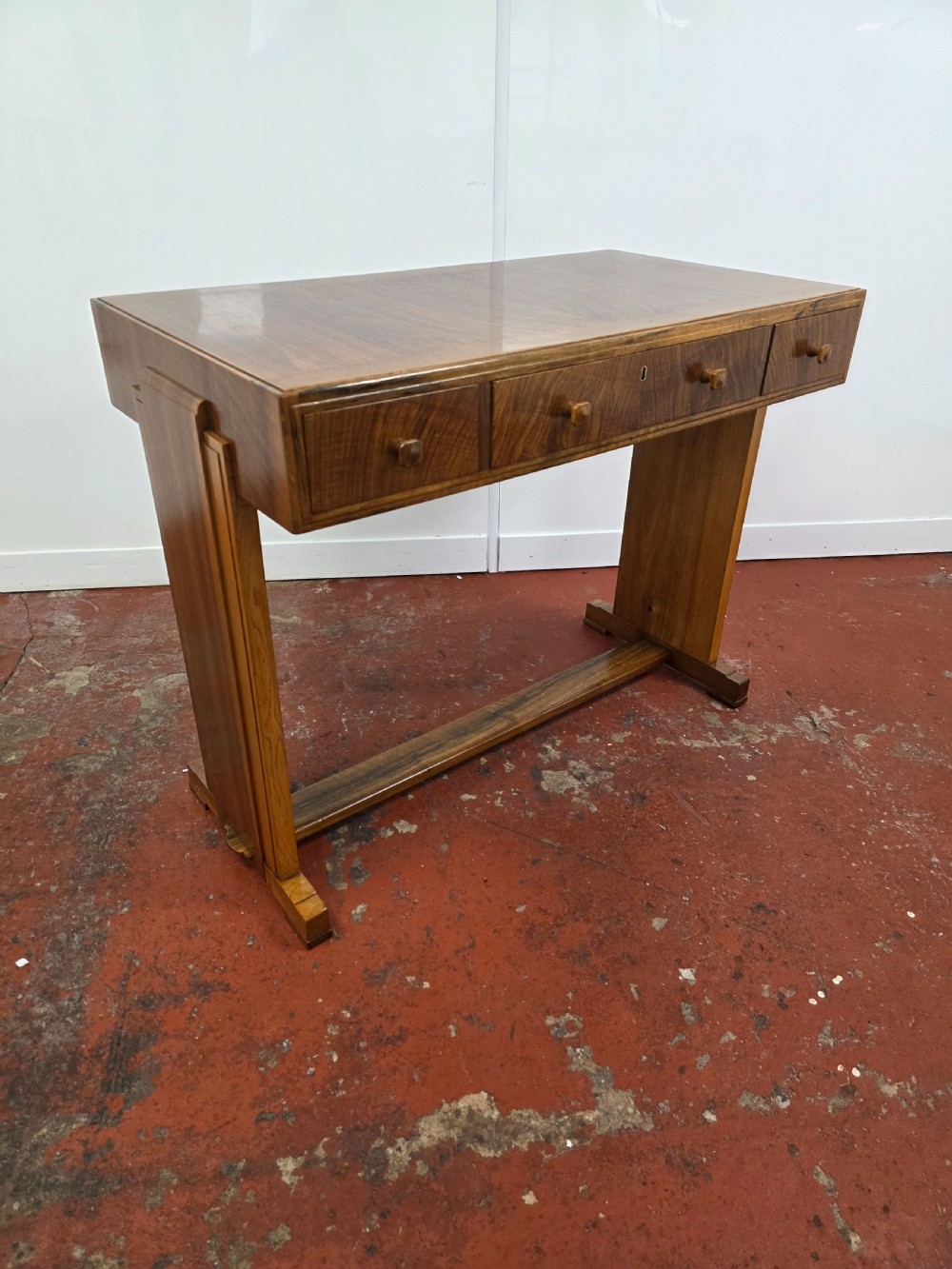A 1930s Art Deco walnut desk featuring a rectangular top with three drawers, flat slab-style end legs, and a low cross stretcher. View III