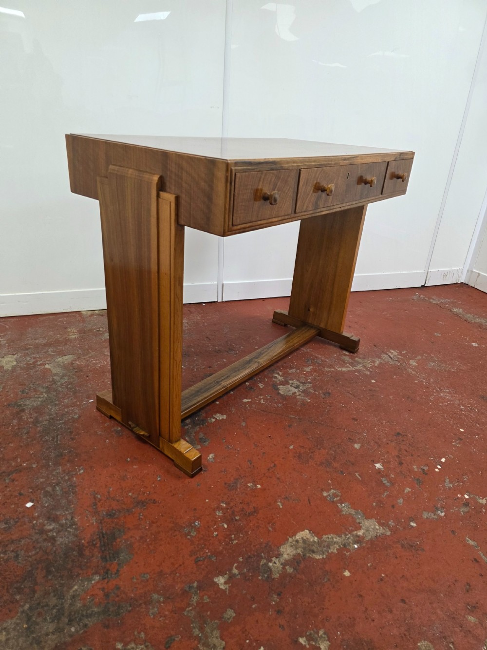 A 1930s Art Deco walnut desk featuring a rectangular top with three drawers, flat slab-style end legs, and a low cross stretcher. View IV